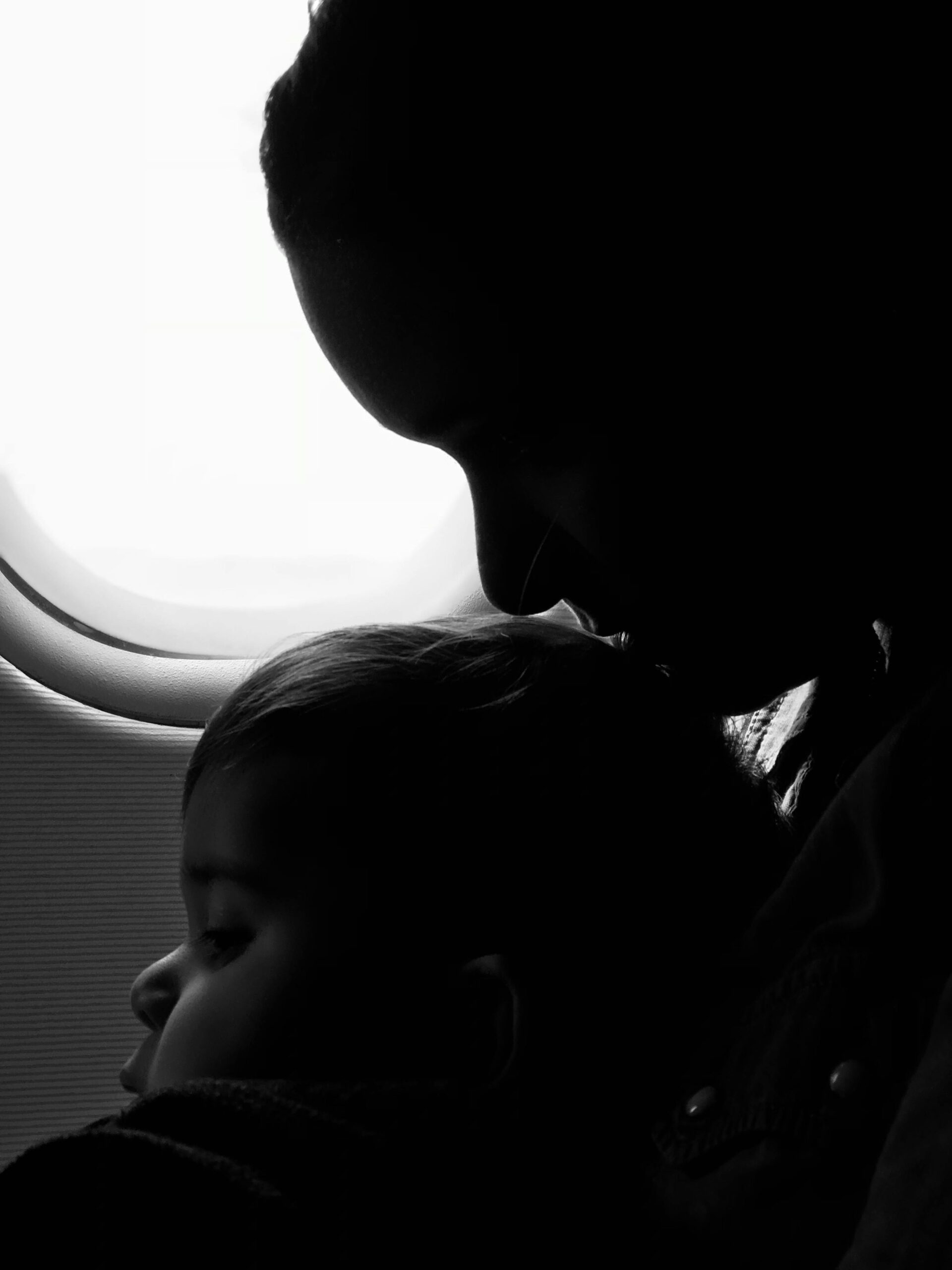 PORUKA ZA TEBE, MAMA Silhouette of a mother and child gazing out an airplane window during flight.